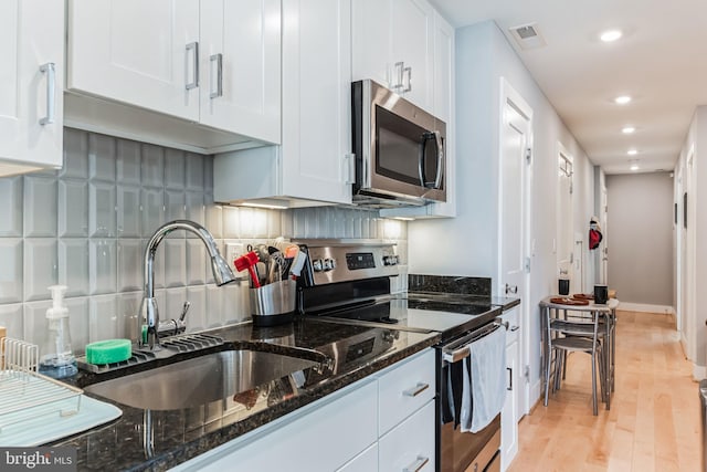 kitchen featuring dark stone counters, white cabinetry, light hardwood / wood-style flooring, and stainless steel appliances