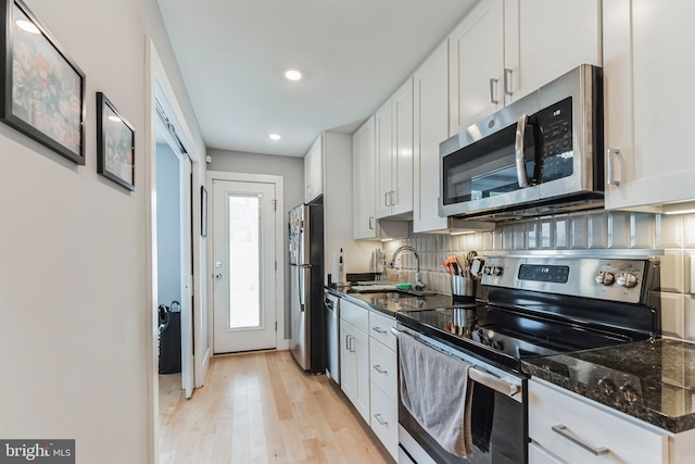 kitchen featuring dark stone countertops, stainless steel appliances, light wood-type flooring, and white cabinetry