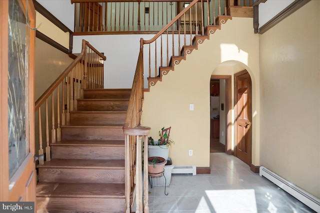 staircase with a towering ceiling and a baseboard heating unit