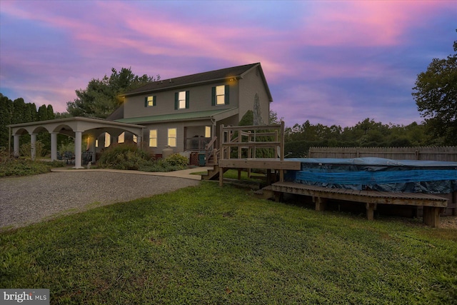 back house at dusk featuring a covered pool and a lawn