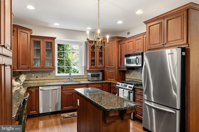 kitchen with light wood-type flooring, a center island, stainless steel appliances, dark stone countertops, and sink