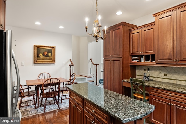 kitchen with a kitchen island, tasteful backsplash, stainless steel refrigerator, dark hardwood / wood-style flooring, and an inviting chandelier