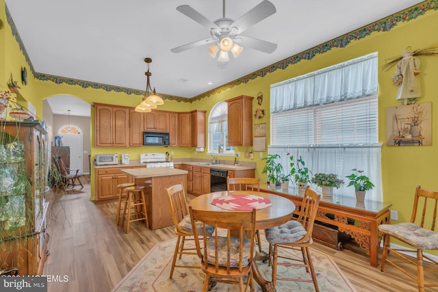 kitchen with ceiling fan, a kitchen bar, black appliances, light hardwood / wood-style floors, and a center island