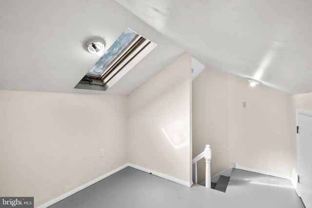 bonus room with lofted ceiling with skylight and concrete flooring