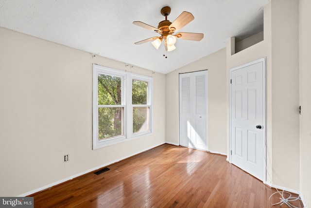 unfurnished bedroom featuring a textured ceiling, a closet, ceiling fan, lofted ceiling, and light hardwood / wood-style flooring