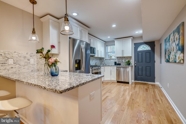 kitchen with appliances with stainless steel finishes, hanging light fixtures, white cabinetry, and kitchen peninsula