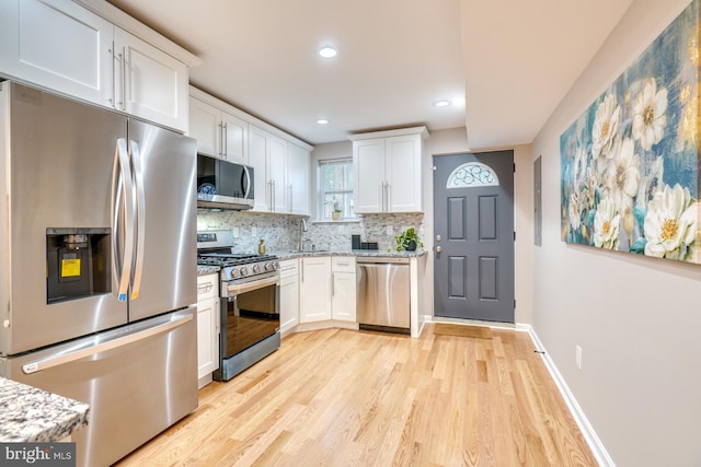 kitchen featuring light stone countertops, light hardwood / wood-style floors, stainless steel appliances, white cabinets, and decorative backsplash