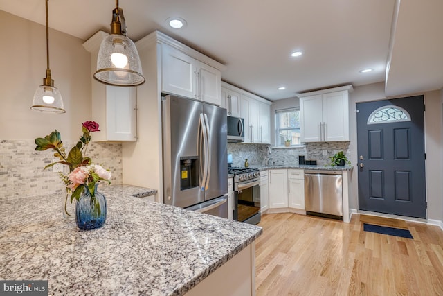 kitchen featuring light hardwood / wood-style flooring, stainless steel appliances, decorative light fixtures, and white cabinets