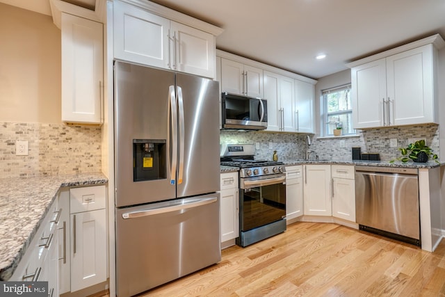 kitchen with light hardwood / wood-style flooring, stainless steel appliances, light stone countertops, white cabinets, and tasteful backsplash