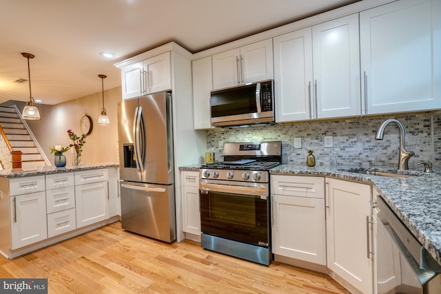 kitchen with hanging light fixtures, white cabinetry, light wood-type flooring, sink, and stainless steel appliances