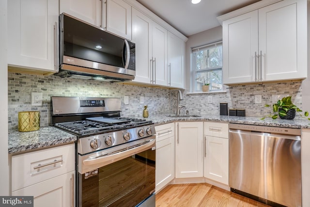 kitchen with sink, white cabinetry, light stone counters, and stainless steel appliances