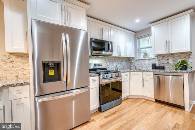 kitchen with backsplash, appliances with stainless steel finishes, light wood-type flooring, and white cabinets