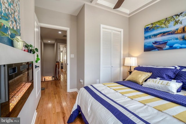 bedroom with a closet, wood-type flooring, crown molding, and ceiling fan