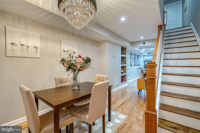 dining area with built in features, a notable chandelier, and light wood-type flooring