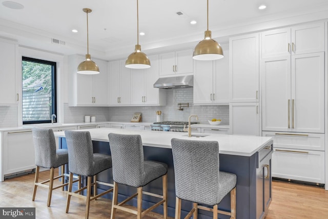 6019 Utah Ave NW, Washington, DC 20015 - kitchen with under cabinet range hood, white cabinetry, light countertops, a center island with sink, and crown molding