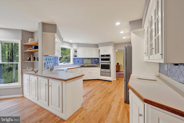 kitchen with stainless steel appliances, backsplash, light hardwood / wood-style flooring, and white cabinetry