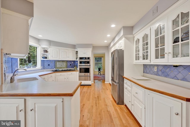 kitchen with sink, kitchen peninsula, light hardwood / wood-style flooring, white cabinetry, and stainless steel appliances