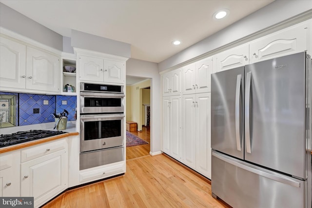 kitchen with stainless steel appliances, backsplash, white cabinets, and light wood-type flooring