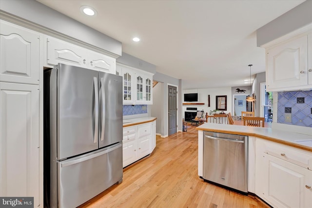 kitchen with decorative backsplash, light hardwood / wood-style floors, white cabinetry, appliances with stainless steel finishes, and decorative light fixtures