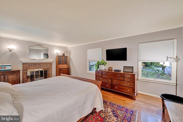 bedroom featuring multiple windows, crown molding, a fireplace, and light hardwood / wood-style floors