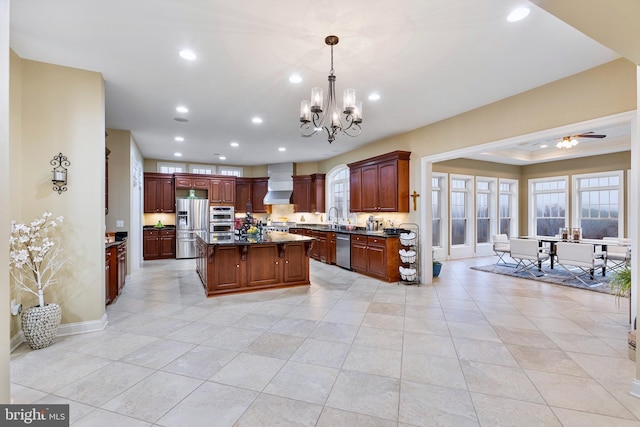 kitchen with appliances with stainless steel finishes, wall chimney exhaust hood, ceiling fan with notable chandelier, sink, and decorative light fixtures