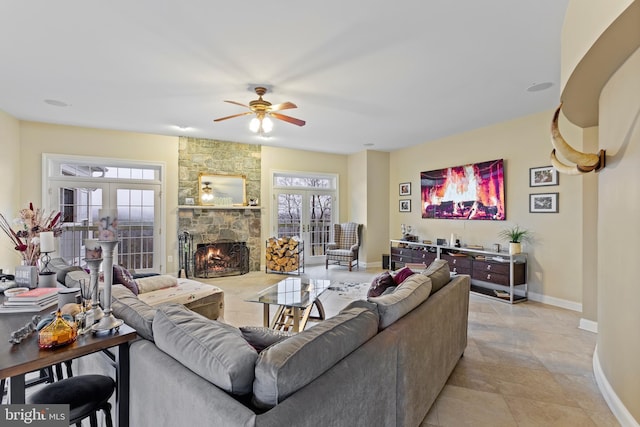 living room featuring french doors, a stone fireplace, ceiling fan, and a healthy amount of sunlight