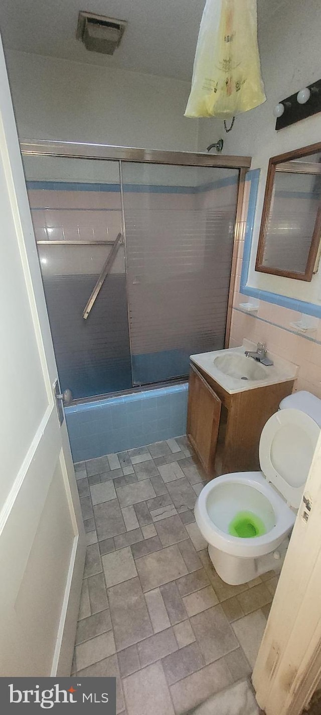 bathroom featuring vanity, enclosed tub / shower combo, and tile walls