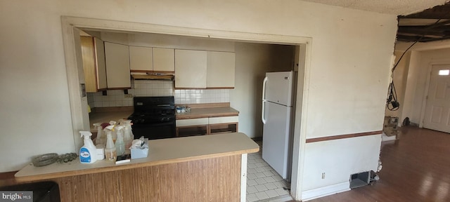 kitchen with stove, backsplash, cream cabinets, kitchen peninsula, and white fridge