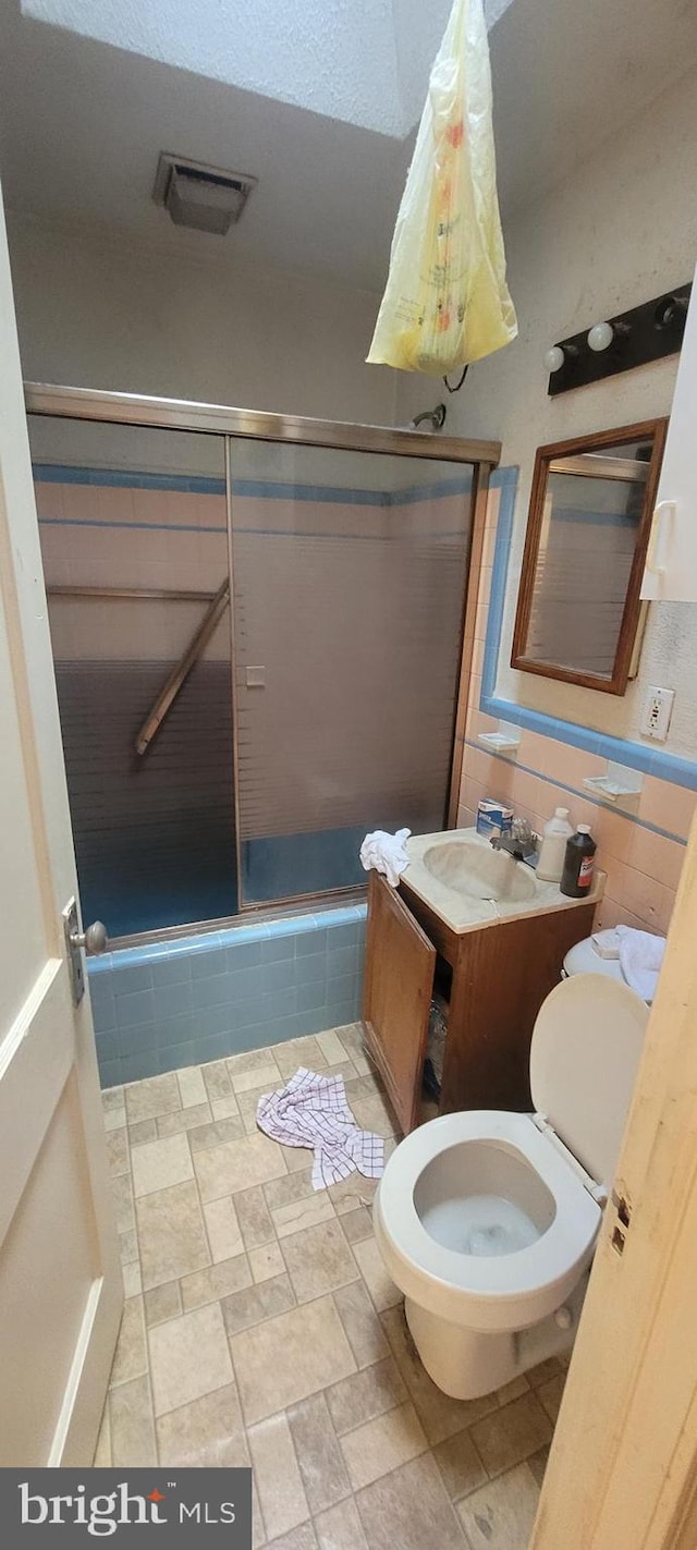 full bathroom featuring enclosed tub / shower combo, tile walls, vanity, and toilet