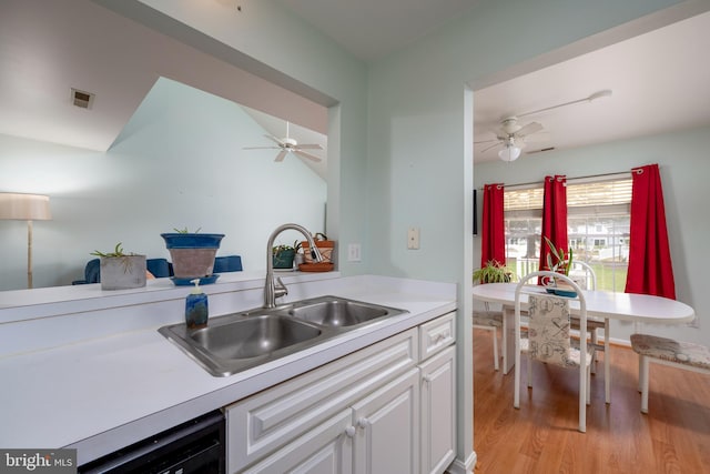 kitchen with light wood-type flooring, ceiling fan, black dishwasher, sink, and white cabinetry