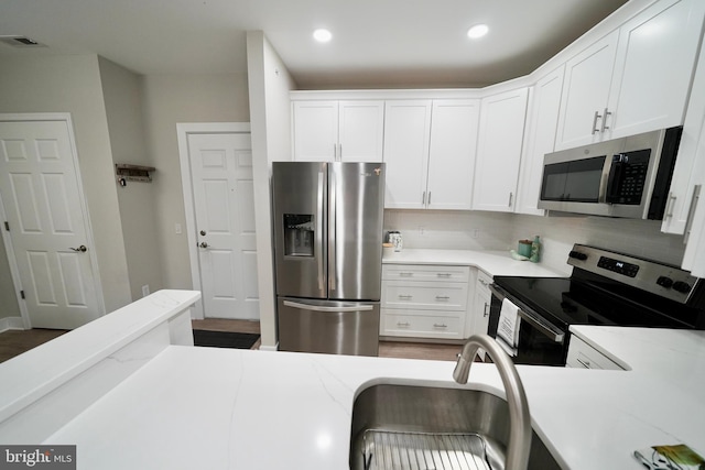 kitchen with backsplash, white cabinetry, stainless steel appliances, and light stone counters