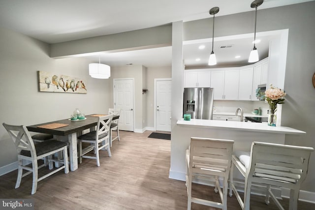 kitchen featuring hardwood / wood-style floors, white cabinets, kitchen peninsula, decorative light fixtures, and stainless steel fridge with ice dispenser