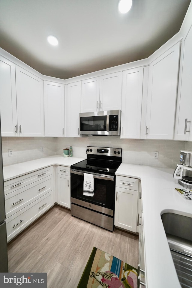 kitchen featuring appliances with stainless steel finishes, backsplash, light hardwood / wood-style floors, and white cabinetry