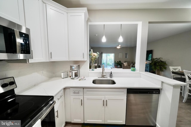 kitchen with kitchen peninsula, appliances with stainless steel finishes, sink, white cabinets, and hanging light fixtures