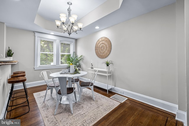 dining area featuring a notable chandelier, dark hardwood / wood-style floors, and a tray ceiling