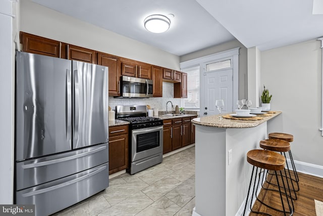 kitchen featuring kitchen peninsula, decorative backsplash, appliances with stainless steel finishes, a kitchen breakfast bar, and sink