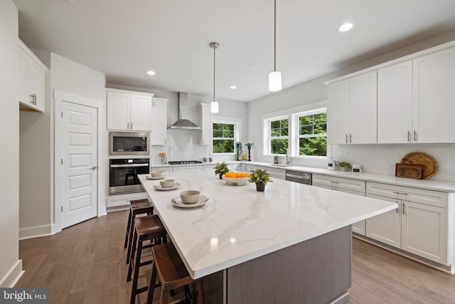 kitchen featuring a kitchen island, white cabinetry, wall chimney range hood, and stainless steel appliances