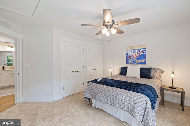 bedroom with connected bathroom, multiple closets, light carpet, and ceiling fan