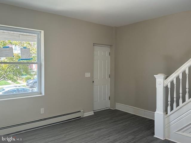 spare room featuring a baseboard heating unit and dark hardwood / wood-style flooring