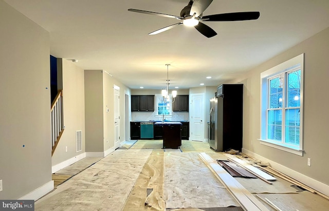 kitchen featuring a center island, backsplash, ceiling fan with notable chandelier, decorative light fixtures, and stainless steel appliances