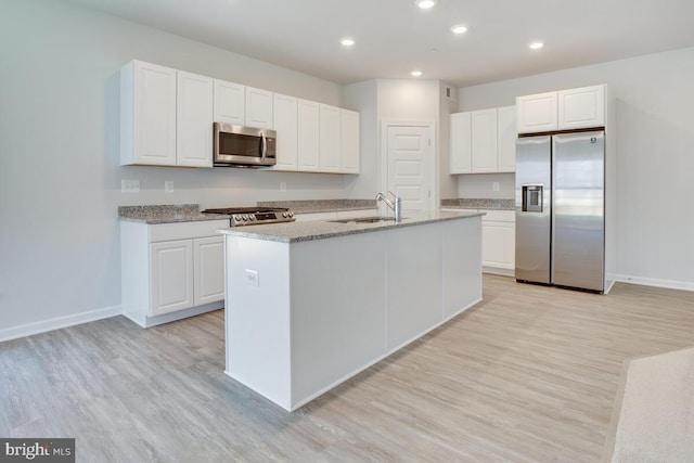 kitchen with white cabinets, an island with sink, stainless steel appliances, and light hardwood / wood-style flooring