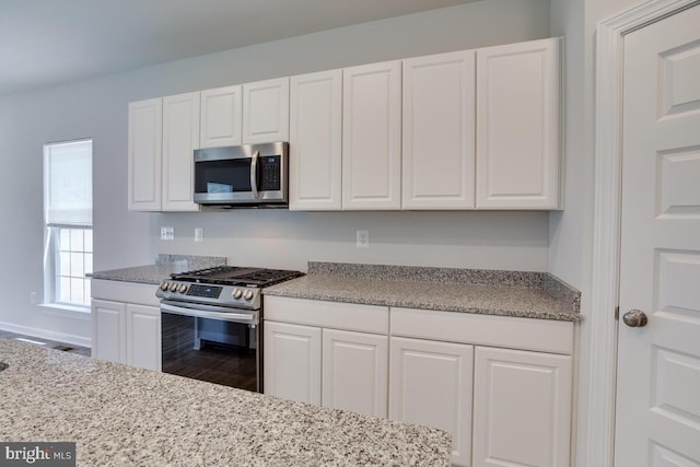 kitchen featuring appliances with stainless steel finishes, hardwood / wood-style flooring, light stone counters, and white cabinetry