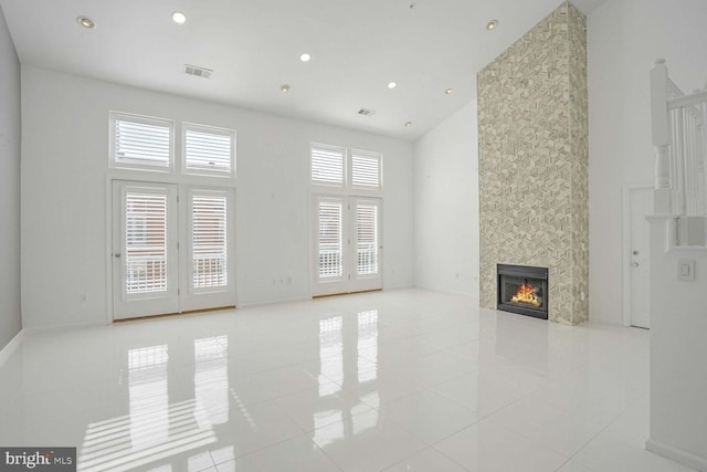 unfurnished living room featuring light tile patterned flooring, a tiled fireplace, a towering ceiling, and plenty of natural light