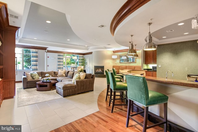 kitchen with a raised ceiling, a breakfast bar area, light hardwood / wood-style flooring, pendant lighting, and crown molding