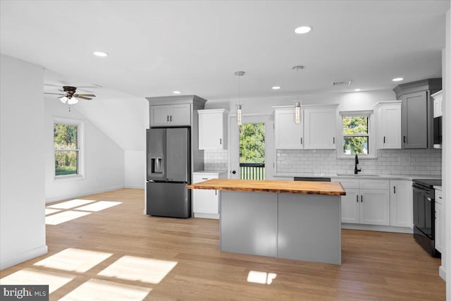 kitchen featuring a healthy amount of sunlight, stainless steel fridge with ice dispenser, hanging light fixtures, and wooden counters