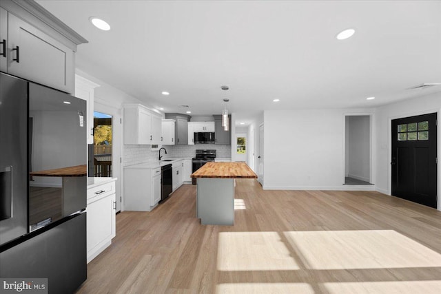 kitchen featuring pendant lighting, a center island, white cabinets, black appliances, and butcher block countertops