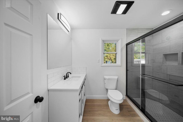 bathroom with backsplash, vanity, hardwood / wood-style floors, toilet, and a shower with shower door