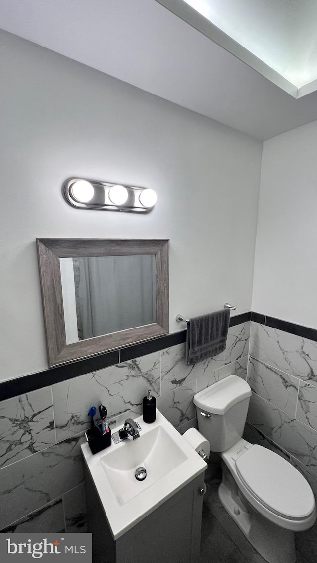 bathroom with vanity, toilet, and tile walls