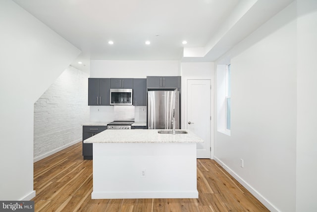 kitchen featuring gray cabinets, appliances with stainless steel finishes, light hardwood / wood-style floors, and an island with sink