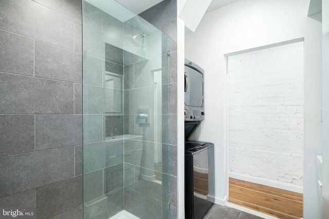 bathroom featuring stacked washer / drying machine, wood finished floors, baseboards, and a tile shower